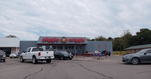 Exterior of a Piggly Wiggly grocery store with parked cars and a cloudy sky in the background.