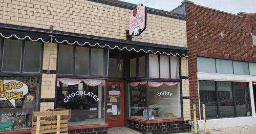 A storefront featuring a sign for chocolates and coffee, with a pink awning and large windows.