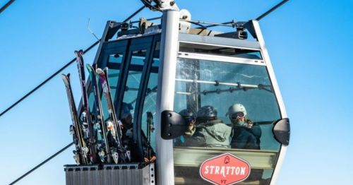 A ski gondola with passengers and skis, set against a clear blue sky at Stratton, Vermont.