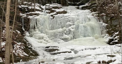 A frozen waterfall surrounded by snow-covered rocks and trees in a winter landscape.
