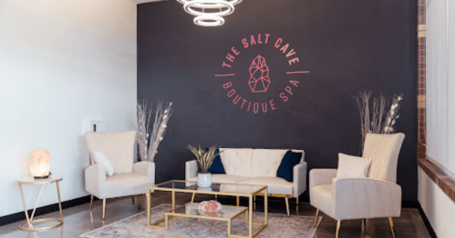 A modern spa lobby featuring two armchairs, a sofa, and a decorative wall with "The Salt Cave Boutique Spa" logo.