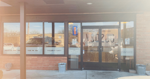 Exterior view of a BBQ restaurant with large glass doors and windows, featuring a sign and a bright blue neon light.