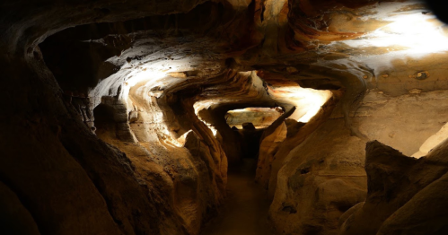 A winding cave with textured rock formations illuminated by soft light, creating a mysterious atmosphere.
