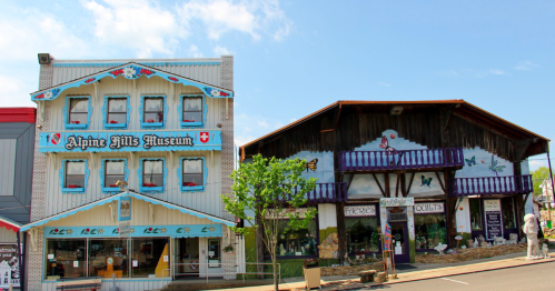Two colorful buildings: the Alpine Hills Museum with decorative trim and a rustic shop with a mural on the right.
