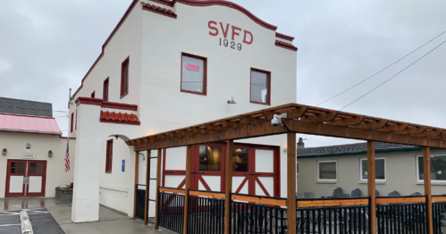 Historic building with "SVFD 1929" sign, featuring a wooden patio and red accents, under a cloudy sky.