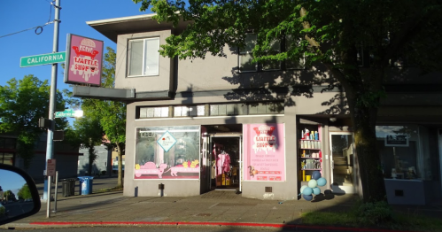 A storefront with a pink sign reading "Waffle Shop," featuring large windows and colorful decor on a sunny day.