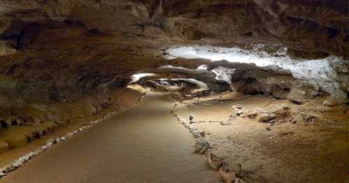 A dimly lit cave interior with a winding path and rocky walls, showcasing natural formations and earthy tones.