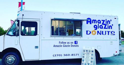 A food truck with "Amazin' Glazin' Donuts" signage, featuring a service window and contact information.