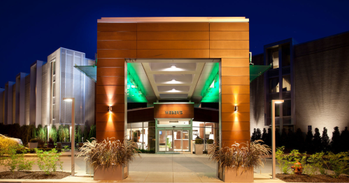 Modern hotel entrance illuminated at night, featuring a sleek design and vibrant green lighting.