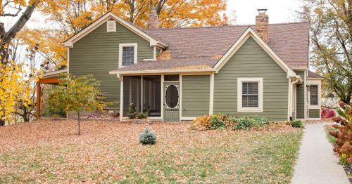 A charming green house surrounded by colorful autumn leaves and trees, with a welcoming front porch.