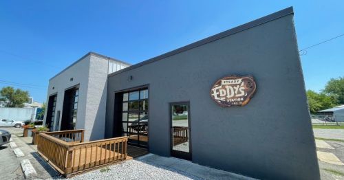 Exterior of a modern building with a sign reading "Eddy's" and a wooden deck in front, under a clear blue sky.