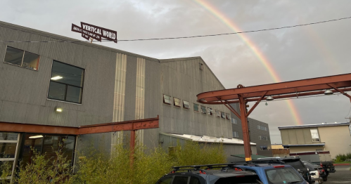 A gray building with a sign reading "Vertical World" and a rainbow in the sky above it.
