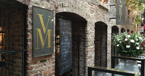 Exterior view of V. Mertz restaurant, featuring brick walls, a sign, and a floral arrangement near the entrance.