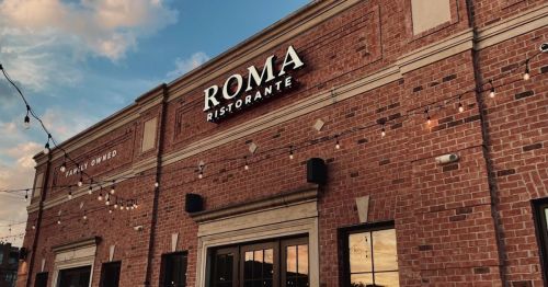 Exterior of Roma Ristorante, a brick building with string lights and a sunset in the background.