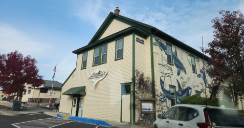 Historic building with a mural, green trim, and a sign. Trees and a parked car are in the foreground.