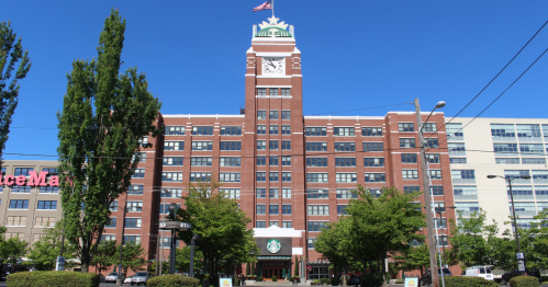 Historic brick building with a green Starbucks sign, surrounded by trees and clear blue sky.