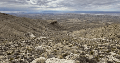 A vast, rugged landscape with rocky hills and sparse vegetation under a cloudy sky.