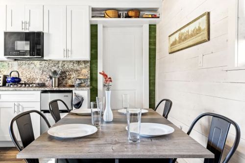 A modern kitchen with a wooden dining table set for four, featuring white plates and a vase of flowers.