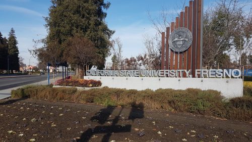 Sign for California State University, Fresno, with landscaped area and trees in the background on a sunny day.