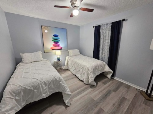 A cozy bedroom with two twin beds, a colorful wall art piece, and a window with dark curtains.