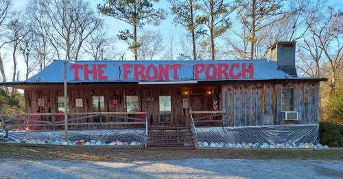 A rustic wooden building with a sign reading "The Front Porch," surrounded by trees and gravel.