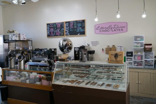 A cozy chocolate shop interior featuring a display case of chocolates, a coffee station, and a chalkboard menu.