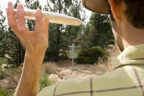 A person prepares to throw a disc towards a disc golf basket in a wooded area.