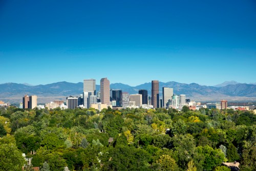 A panoramic view of a city skyline surrounded by greenery and mountains under a clear blue sky.