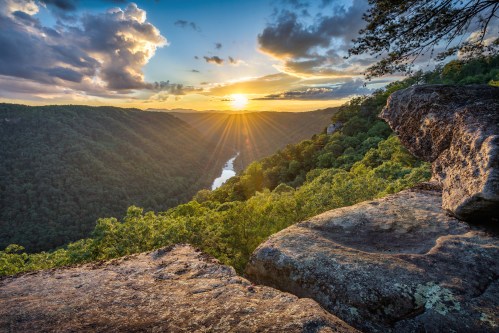 A stunning sunset over a lush valley, with a river winding through the landscape and clouds scattered in the sky.