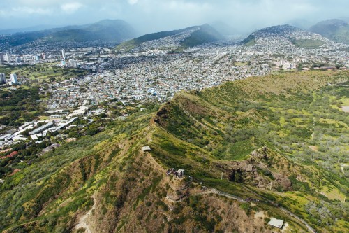 Aerial view of a lush green mountain ridge overlooking a cityscape with hills in the background.