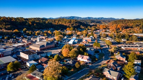 Aerial view of a small town surrounded by mountains, showcasing autumn foliage and a mix of buildings and streets.