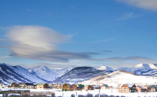 Snow-covered mountains rise behind a small village with colorful houses under a clear blue sky.