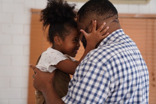 A joyful father and daughter share a playful moment, smiling and touching foreheads in a warm, loving embrace.