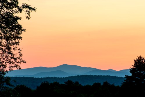 Silhouetted mountains against a pastel sunset sky, framed by trees in the foreground.
