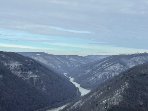 A scenic view of a winding river surrounded by snow-covered mountains under a cloudy sky.