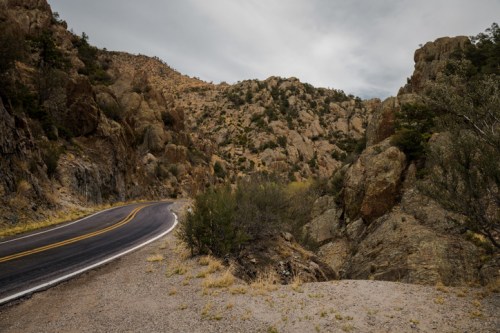 Winding road through rocky terrain with sparse vegetation under a cloudy sky.