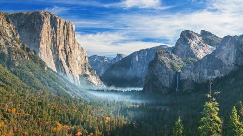 A stunning view of Yosemite Valley, featuring towering cliffs, lush forests, and a waterfall under a blue sky.