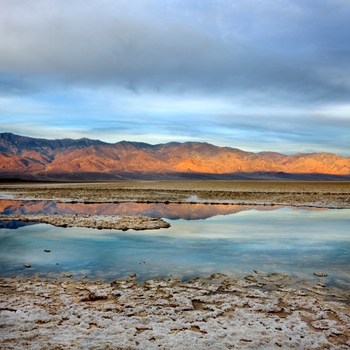 A serene landscape featuring a salt flat with a reflective pool and mountains under a clear blue sky.