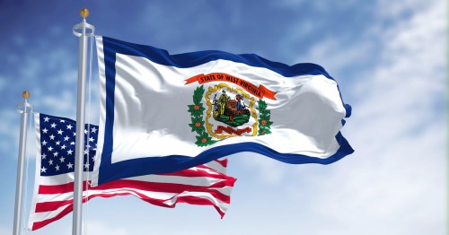 The flags of West Virginia and the United States waving against a blue sky.