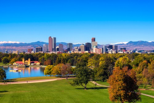 A vibrant city skyline with mountains in the background, surrounded by colorful trees and a serene lake.