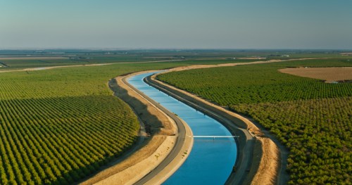 Aerial view of a winding river bordered by lush green fields under a clear sky.