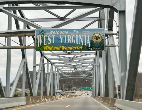 A welcome sign for West Virginia on a bridge, featuring the slogan "Wild and Wonderful" and the state seal.