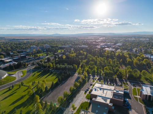 Aerial view of a green campus with buildings, trees, and mountains in the distance under a bright blue sky.