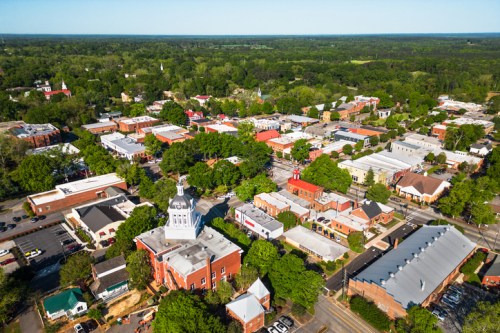 Aerial view of a small town with green trees, shops, and a historic building in the foreground.