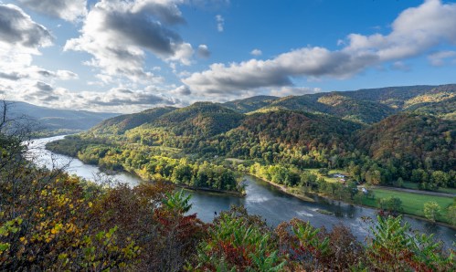 A scenic view of a river winding through lush green hills under a partly cloudy sky.