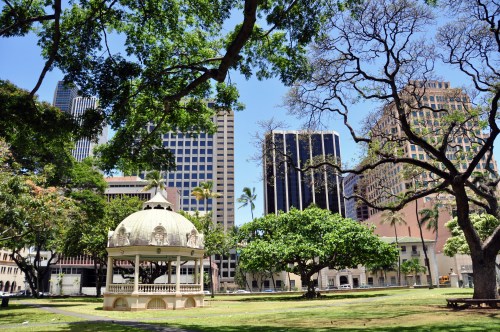 A gazebo surrounded by trees and tall buildings in a sunny park setting.