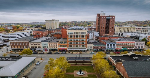 Aerial view of a downtown area with historic buildings, shops, and autumn trees under a cloudy sky.