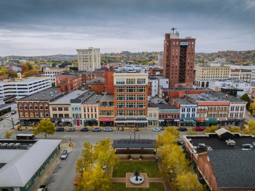 Aerial view of a downtown area with historic buildings, trees, and a park, under a cloudy sky.