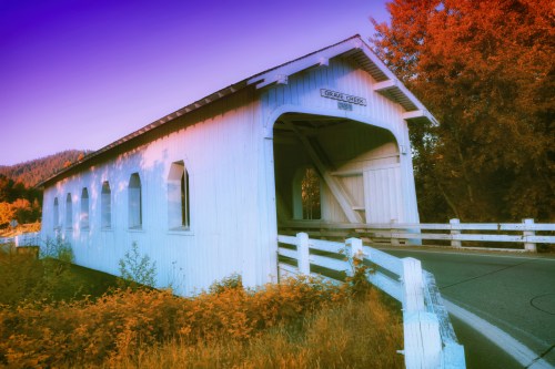 A white covered bridge surrounded by vibrant autumn foliage and a clear blue sky.