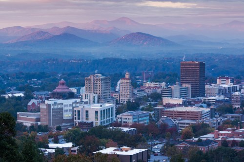 A panoramic view of a city skyline surrounded by mountains at dawn, with soft purple and blue hues in the sky.